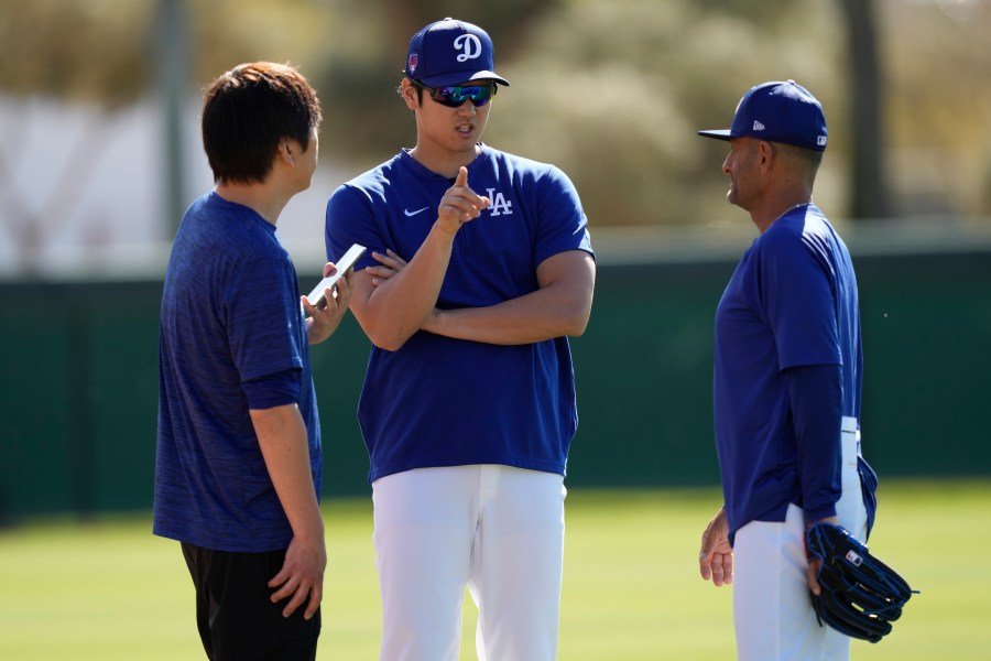 Los Angeles Dodgers' Shohei Ohtani, center, with interpreter Ippei Mizuhara, left, talks with coach Dino Ebel, right, during spring training baseball workouts at Camelback Ranch in Phoenix, Sunday, March 3, 2024. (AP Photo/Carolyn Kaster)