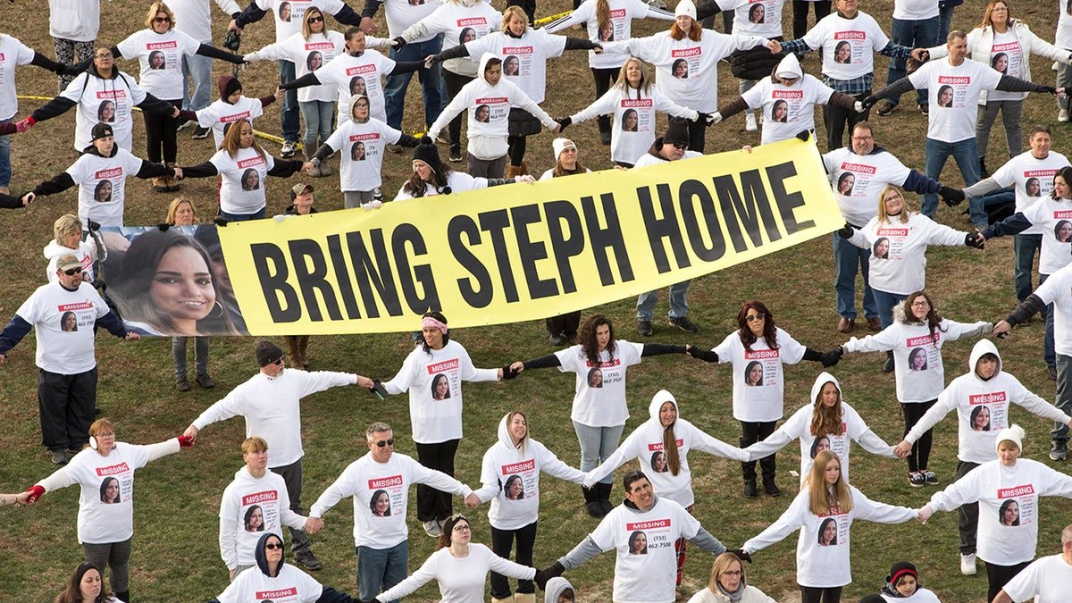 Volunteers holding hands with a banner that reads bring Steph home