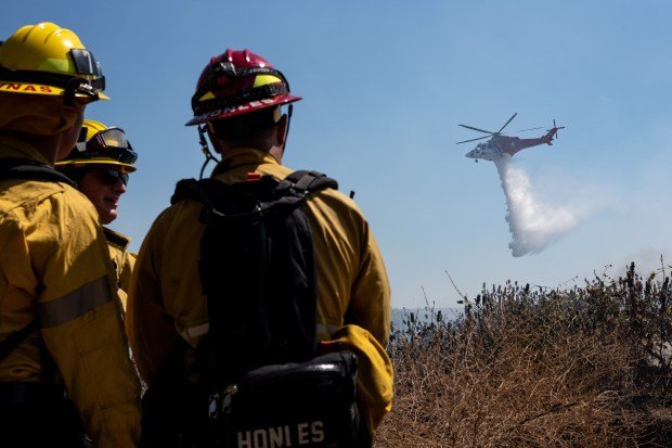 Firefighters look on as a helicopter makes a water drop...
