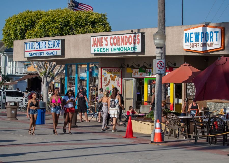 NEWPORT BEACH, CA - JULY 20: People walk, ride and skateboard on the sidewalk past businesses near the pier on a summer day Monday, July 20, 2020 in Newport Beach, CA. (Allen J. Schaben / Los Angeles Times via Getty Images)