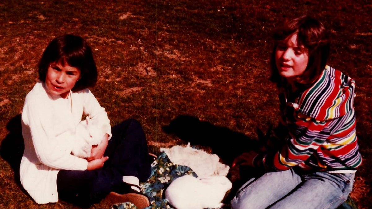 Jonelle Matthews wearing white sitting next to her sister who is wearing a multicolored sweater.