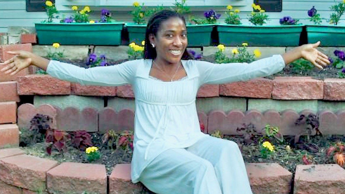 Genai Coleman with her arms outstretched in white sitting in a garden