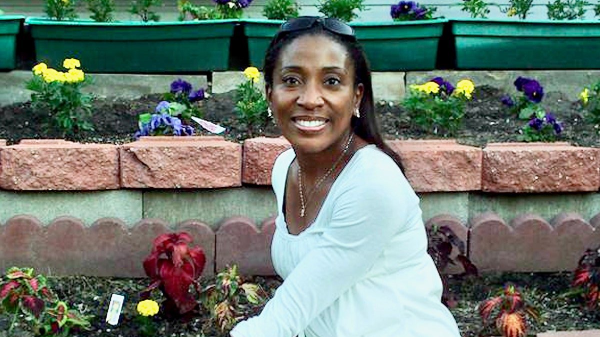 Genai Coleman smiling in white sitting in a garden.